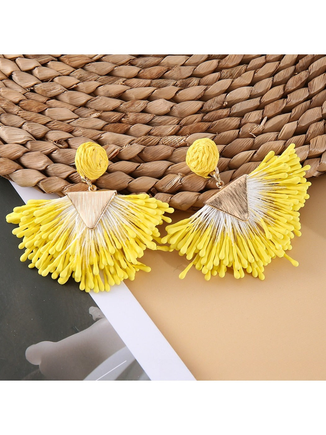 Earedge fan-shaped raffia earrings hanging from a jewelry stand