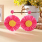 Pair of sunflower-shaped raffia earrings hanging from a jewelry stand