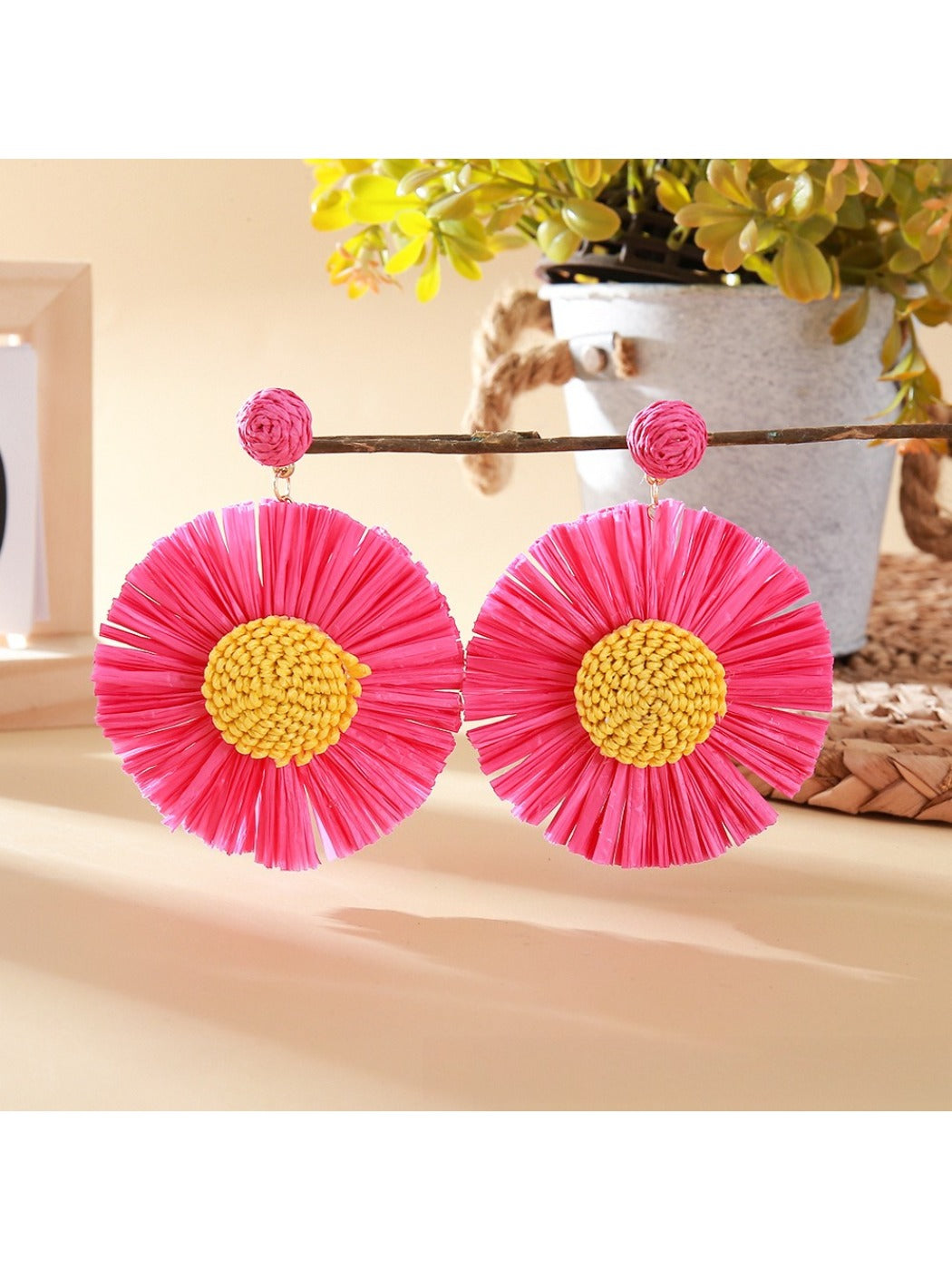 Pair of sunflower-shaped raffia earrings hanging from a jewelry stand