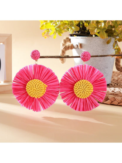 Pair of sunflower-shaped raffia earrings hanging from a jewelry stand