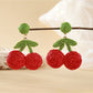 Model wearing raffia woven cherry shaped earrings with green leaves
