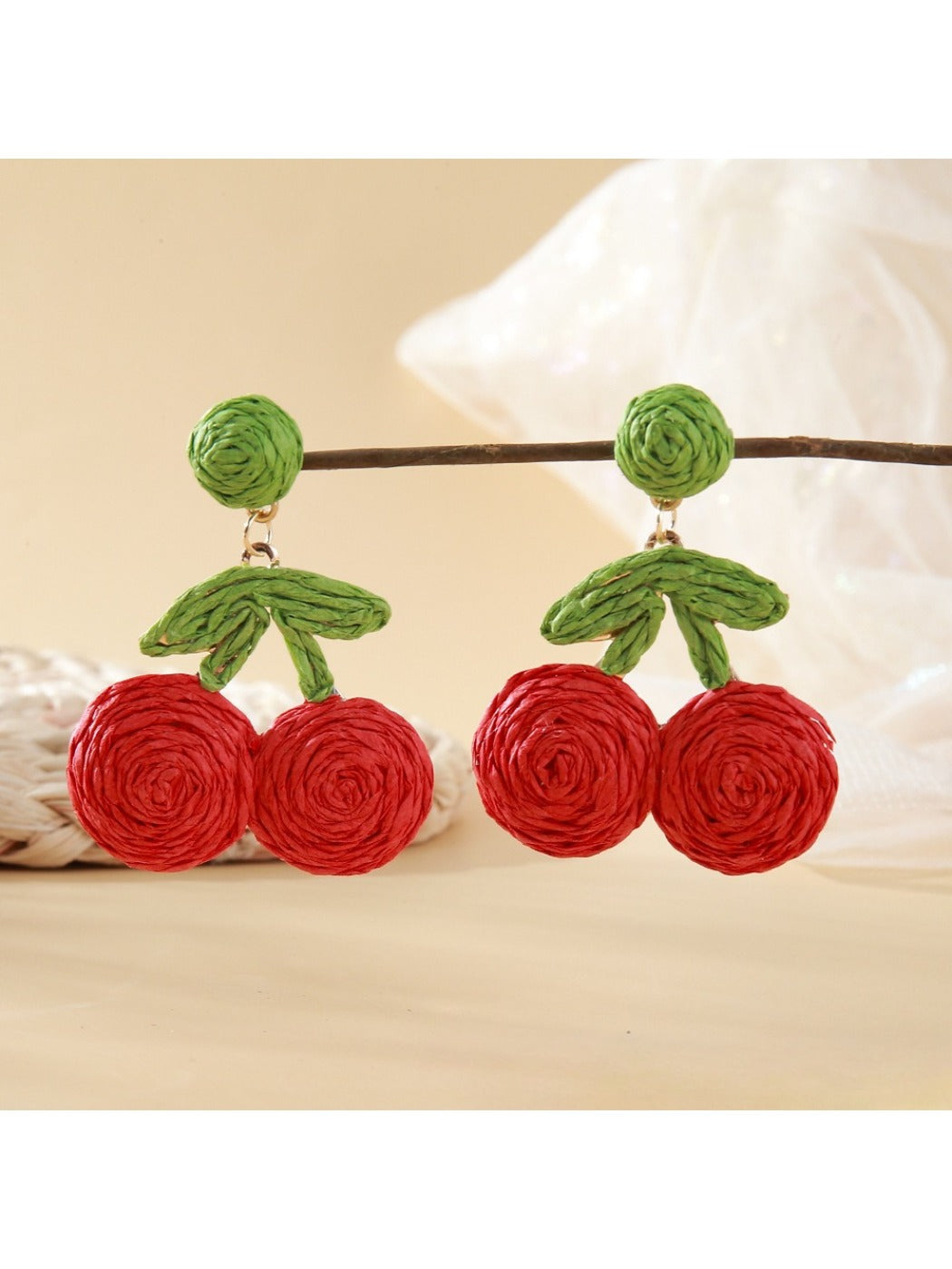 Model wearing raffia woven cherry shaped earrings with green leaves