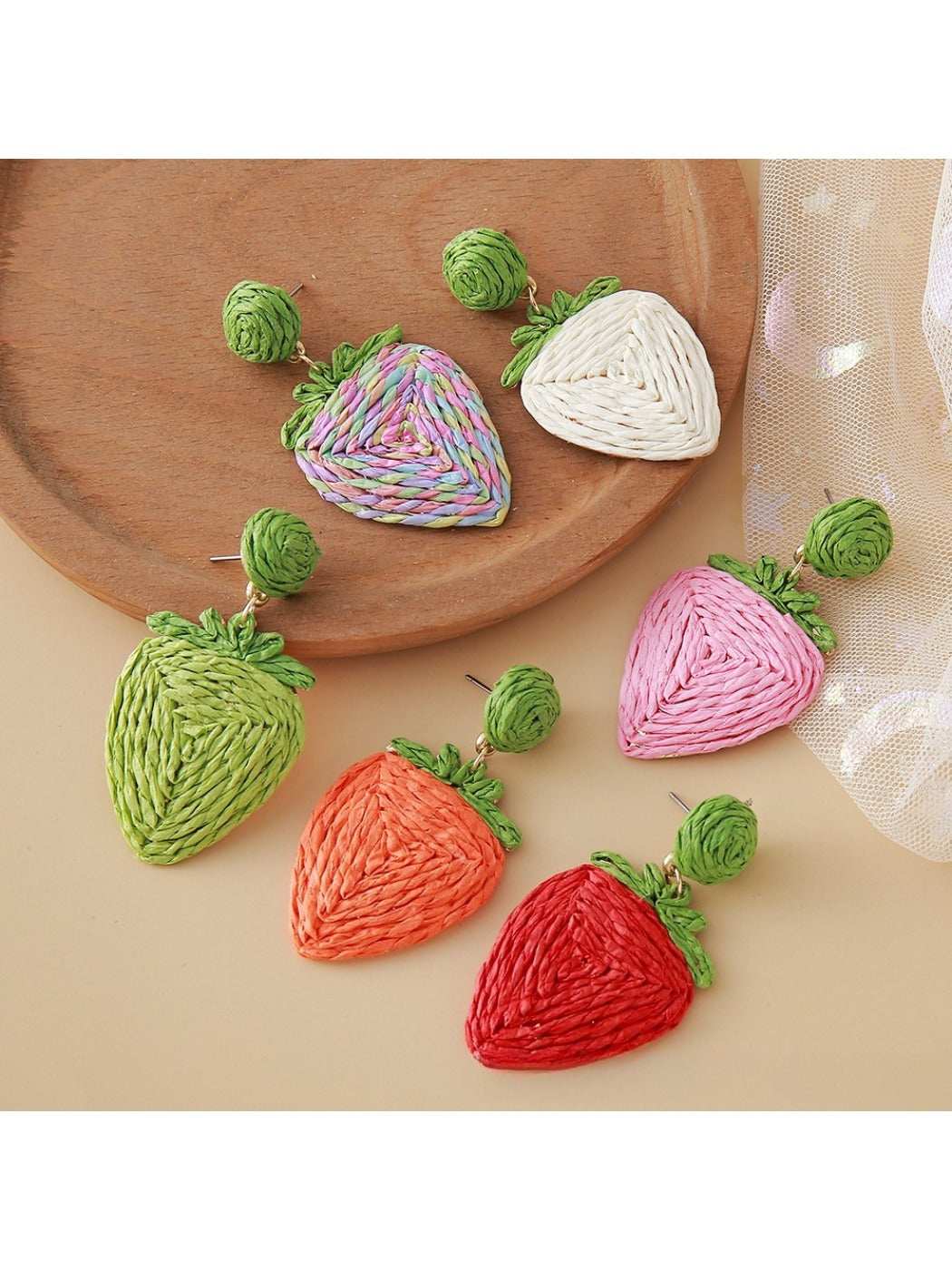 Close-up of raffia woven strawberry-shaped earrings with green leaf details