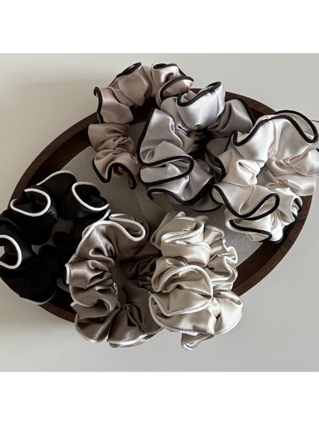 Side view of pink ruffled satin scrunchie showing fabric folds and sheen