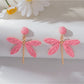 Raffia dragonfly earrings placed on natural wood surface