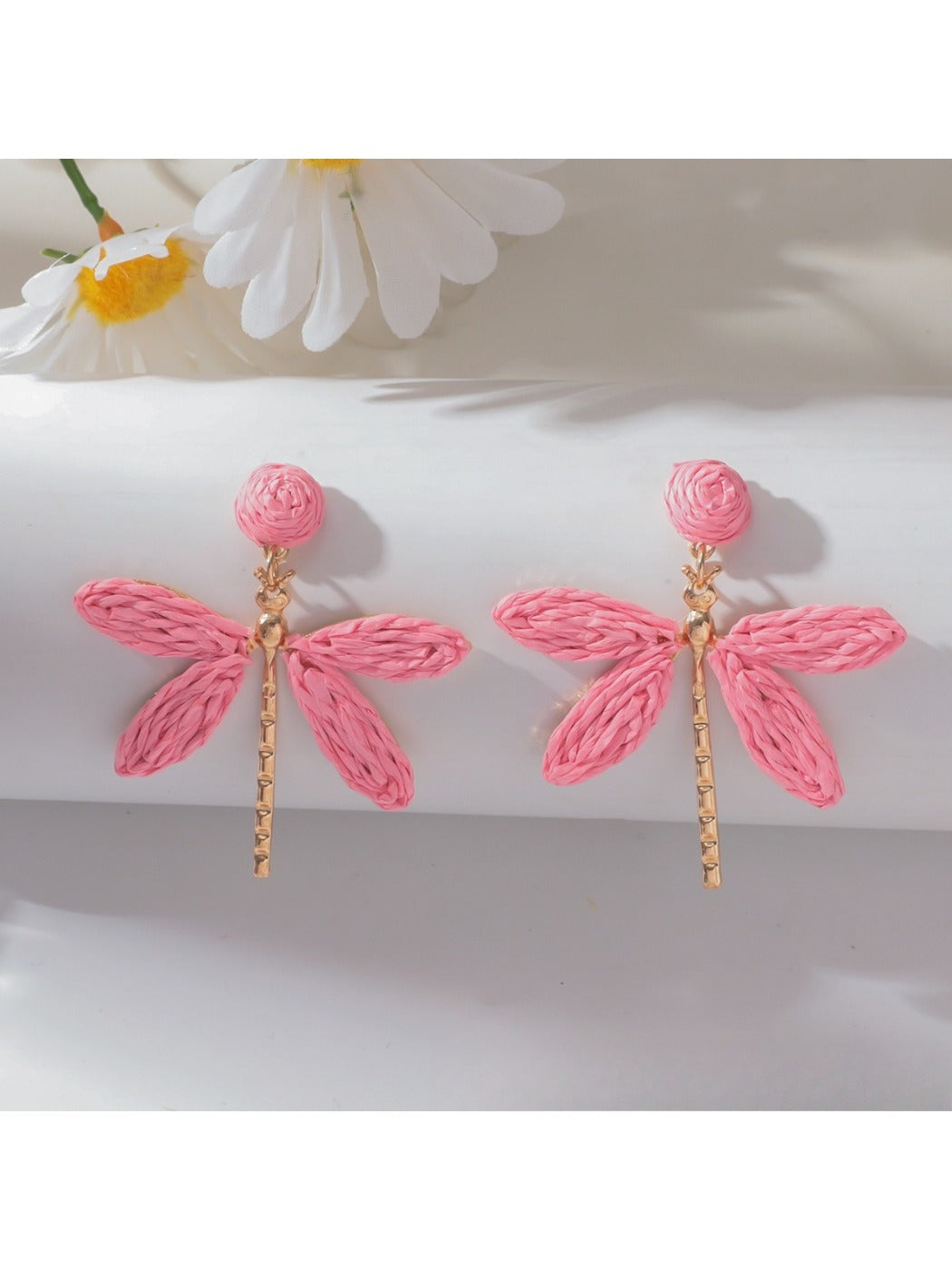Raffia dragonfly earrings placed on natural wood surface