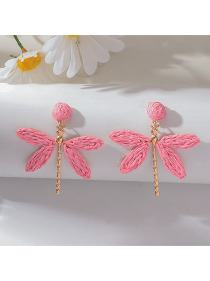 Raffia dragonfly earrings placed on natural wood surface