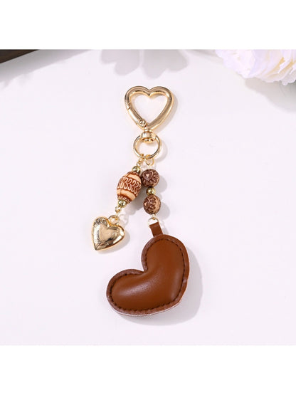 Brown leather heart keychain hanging from a bag strap outdoors