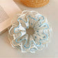 Gifty floral ruffled scrunchie styled on a wrist showing soft fabric texture and floral pattern