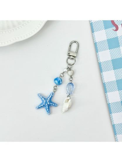 Starfish pendant keychain next to a seashell for size comparison