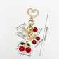 Keypus cherry charm keychain hanging from a handbag zipper pull