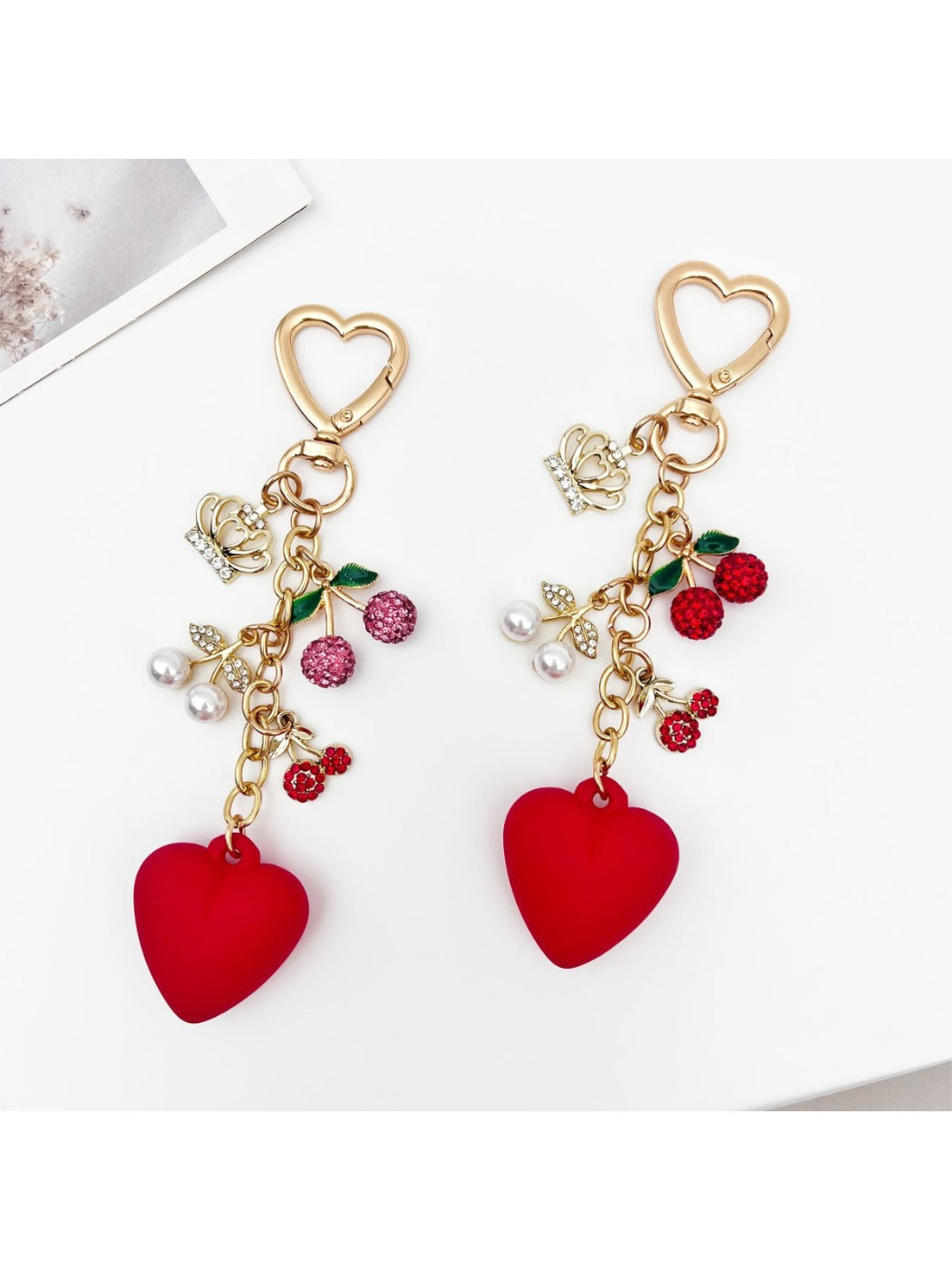 Close-up of cherry heart charm keychain showing detailed red enamel and gold edges