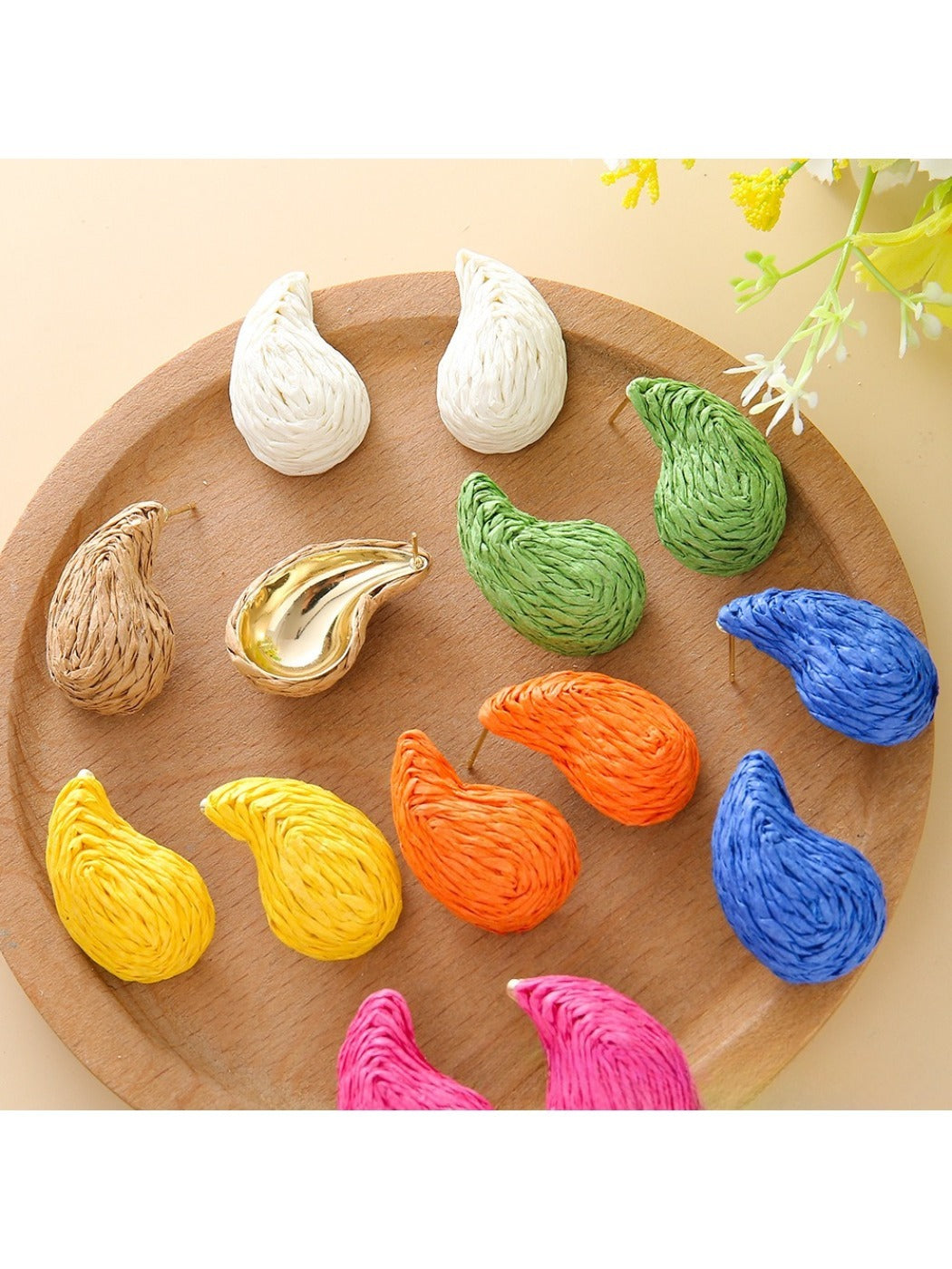 Pair of raffia water drop shaped stud earrings displayed on a wooden surface