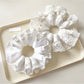 White scrunchie with delicate lace trim on a plain background