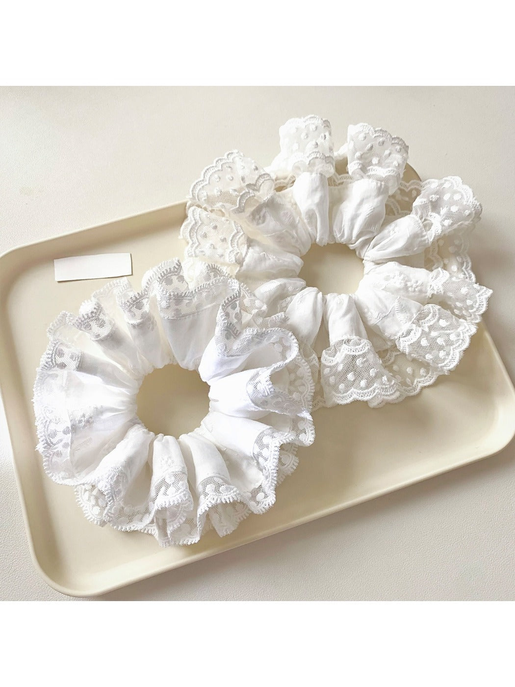 White scrunchie with delicate lace trim on a plain background