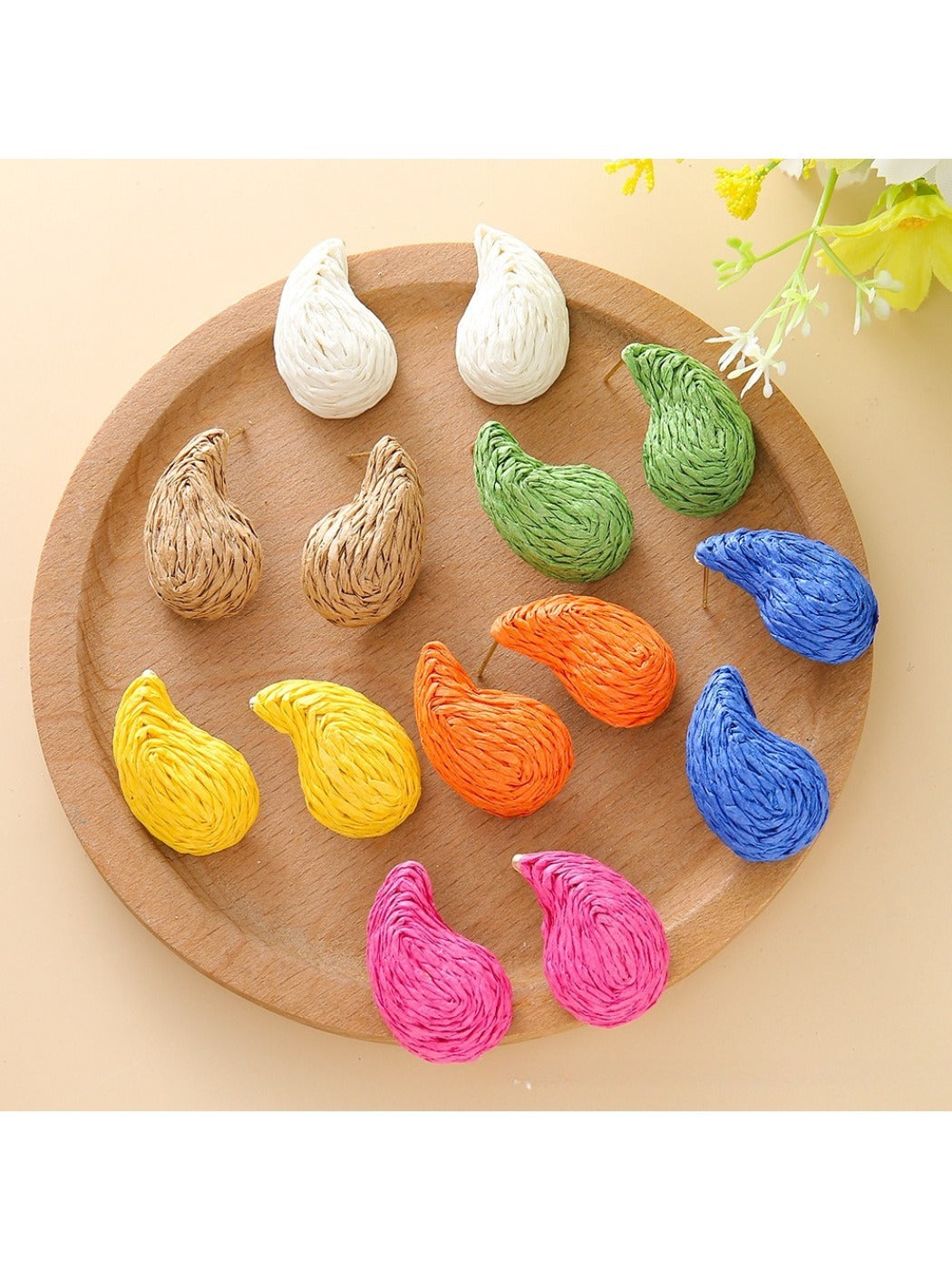 Close-up of Earedge raffia water drop shaped stud earrings on white background