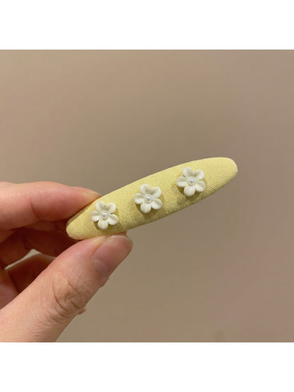 Yellow tiny floral hair clip placed next to matching fabric swatches