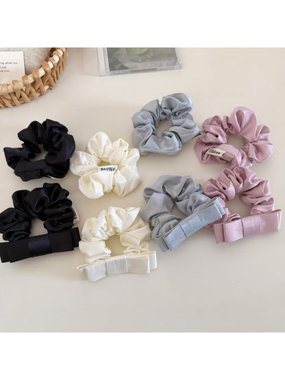 Close-up of a minimalist satin bow scrunchie in soft beige on a white background