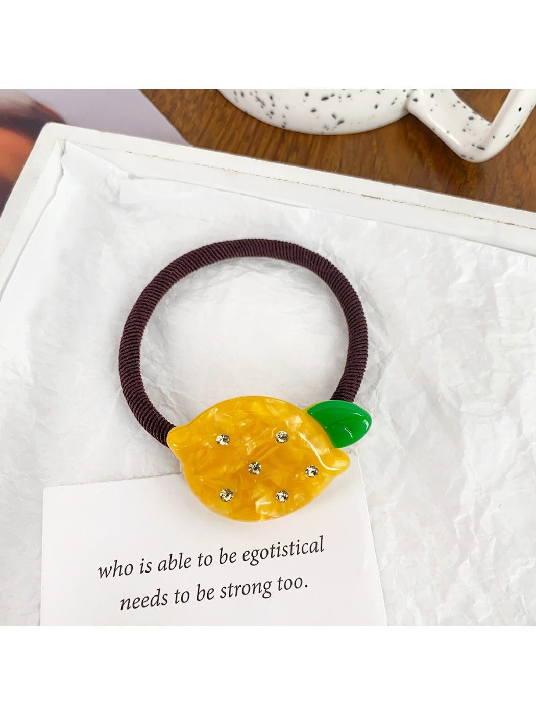Close-up of a yellow hair tie with a lemon charm on a wooden background
