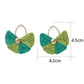 Pair of vintage fan shaped raffia earrings displayed on a wooden surface