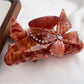 Beau hair claw clip with butterfly design displayed on a fabric surface
