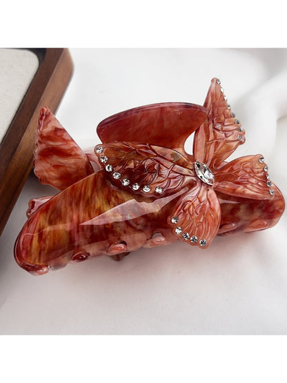 Beau hair claw clip with butterfly design displayed on a fabric surface