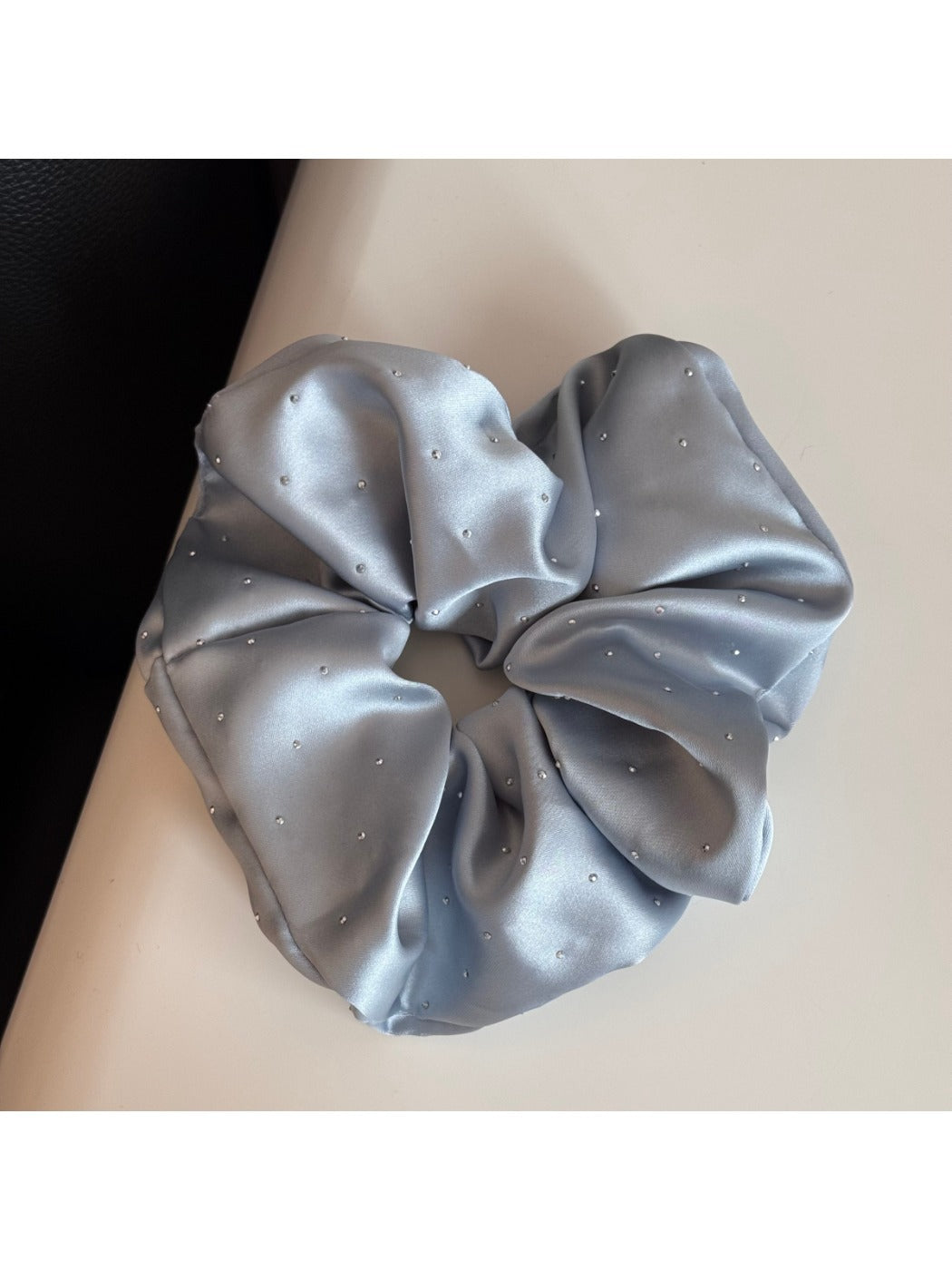 Pink satin scrunchie embellished with rhinestones laid flat on a wooden surface