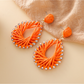 Pair of natural raffia drop earrings with geometric shapes on white background