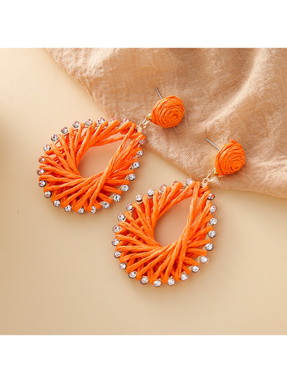 Pair of natural raffia drop earrings with geometric shapes on white background