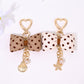 Keypus bow-shaped keychain with white polka dots on a black background