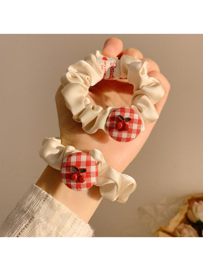 Flat lay of Gifty Sweet Plaid Cherry Hair Tie showing fabric texture and attached cherry charm