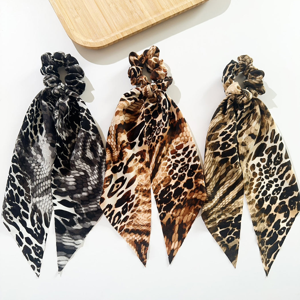 Three snakeskin ribbon bow scrunchies on white background