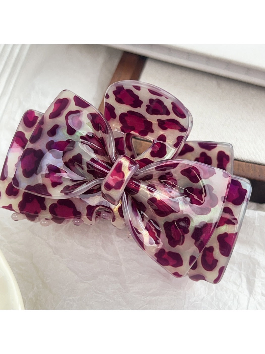 Beau bow-shaped claw clip with leopard print next to green leaves