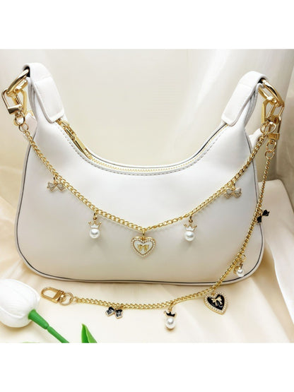 Close-up of gold bow detail on heart pendant bag charm with pink leather background