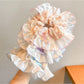 Gifty floral scrunchie stretched around a wrist showing its elasticity and floral pattern