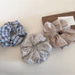Close-up of Gifty plaid scrunchie with beige and black check pattern on white background