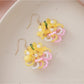 Colorful beaded flower cluster earrings placed next to green leaves for styling