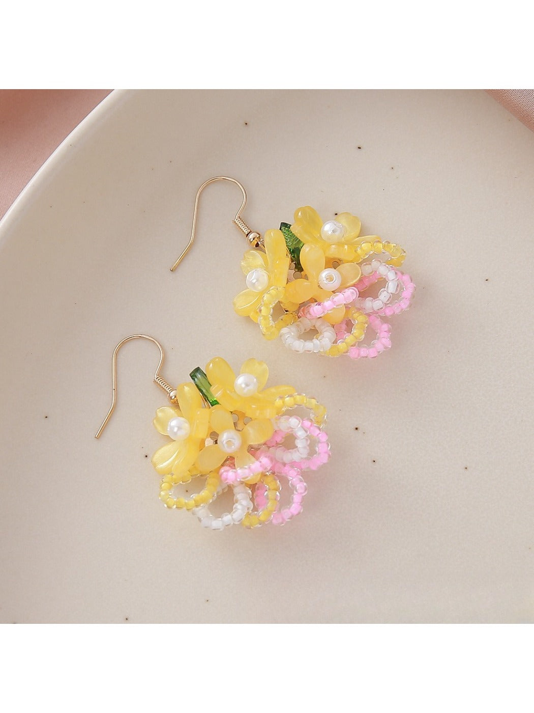 Colorful beaded flower cluster earrings placed next to green leaves for styling