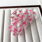 Clear acetate claw clip resting on white surface, side angle