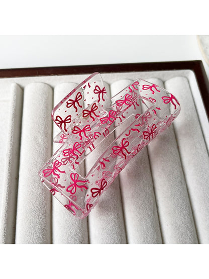 Clear acetate claw clip resting on white surface, side angle