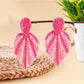 Pair of Earedge raffia woven leaf shaped earrings hanging on a jewelry stand