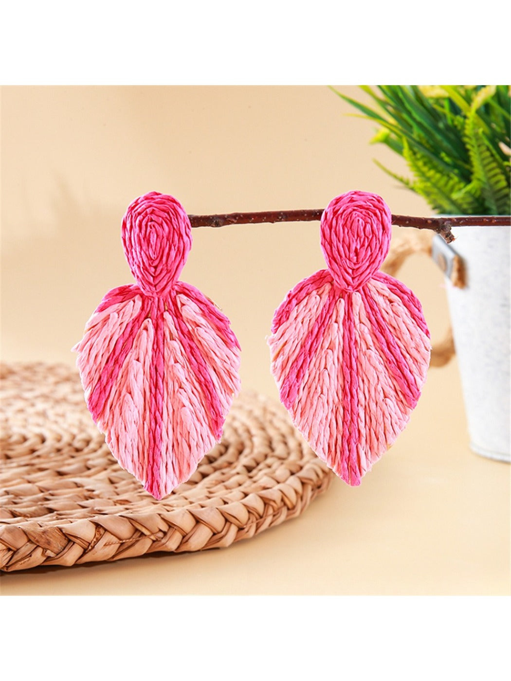 Pair of Earedge raffia woven leaf shaped earrings hanging on a jewelry stand