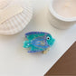 Beau fish claw clip placed on a wooden surface emphasizing vibrant colors