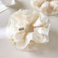 White ruffle scrunchie styled on a model's wrist with soft lighting