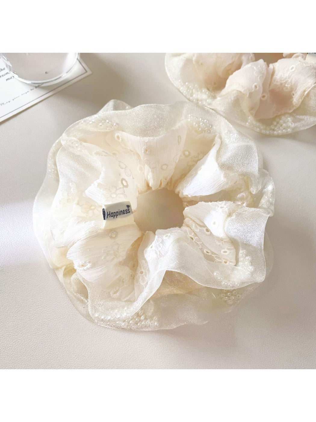 White ruffle scrunchie styled on a model's wrist with soft lighting