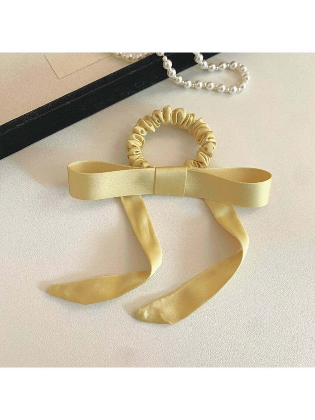 Close-up of Gifty satin yellow ribbon bow scrunchie on white background