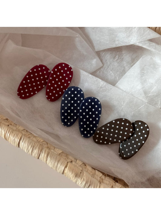 Oval hair clip with white polka dots on a beige background, close-up view