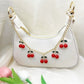 Cherry bag charm hanging from a beige handbag strap