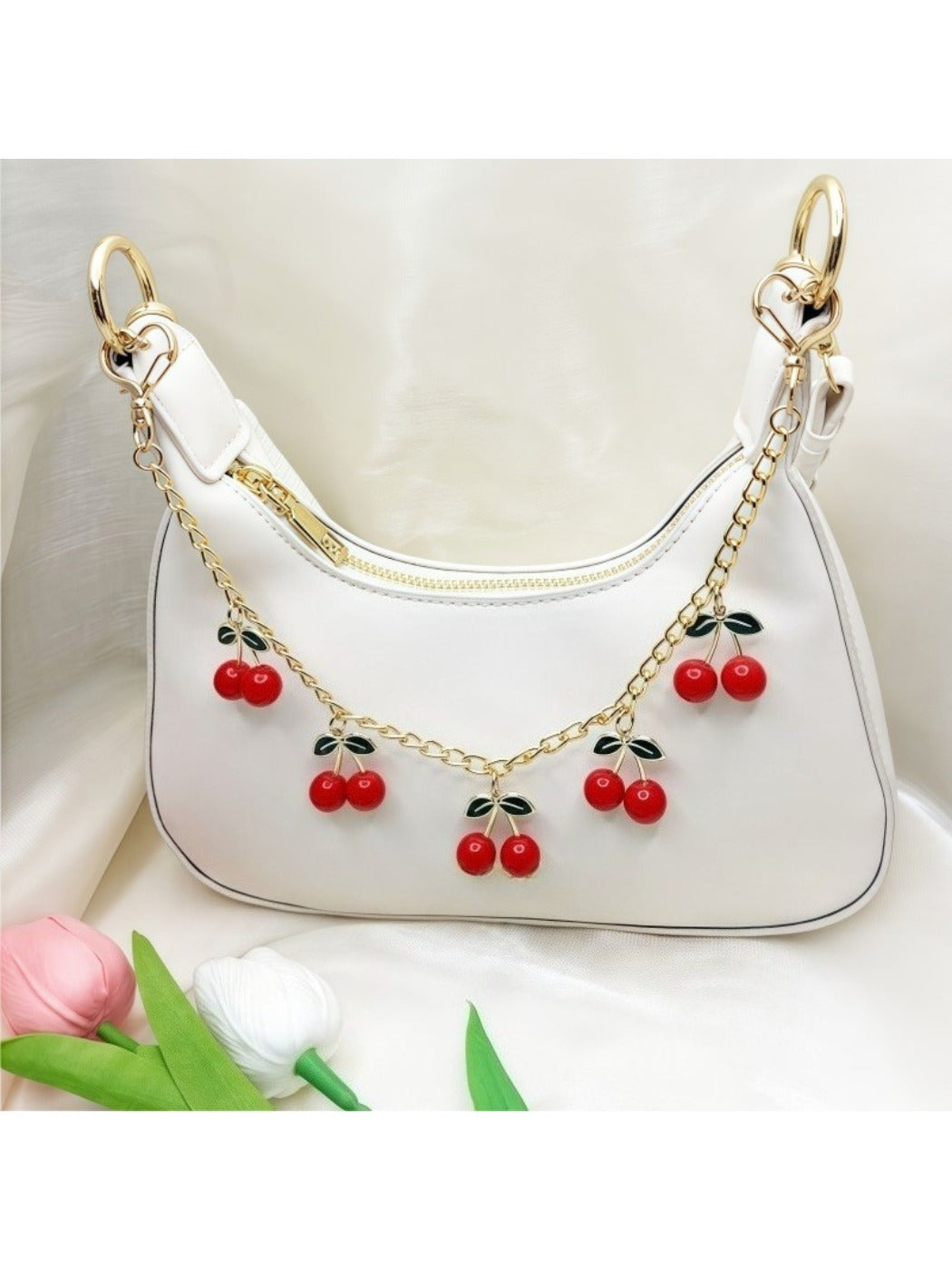 Cherry bag charm hanging from a beige handbag strap