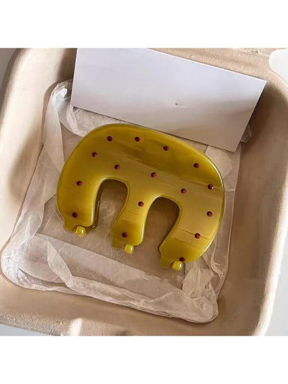 Side view of yellow Beau claw clip with white polka dots on a wooden surface